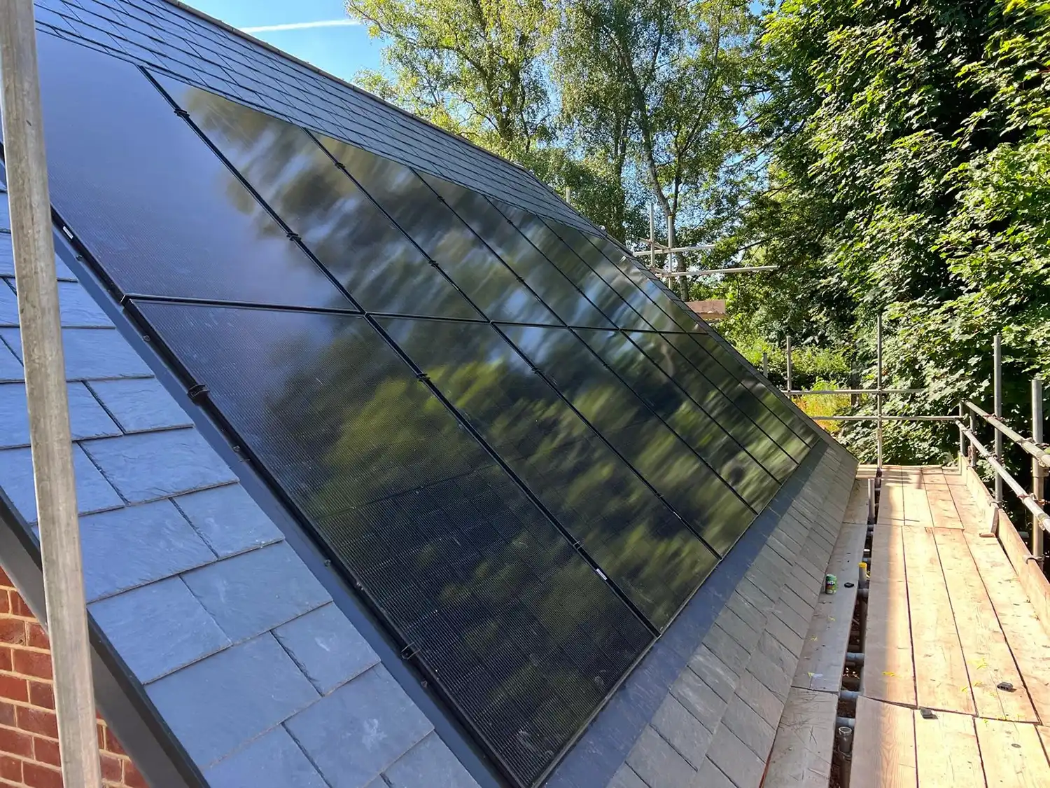 Solar panels installed on a sloped roof with trees and blue sky reflected on the panels.